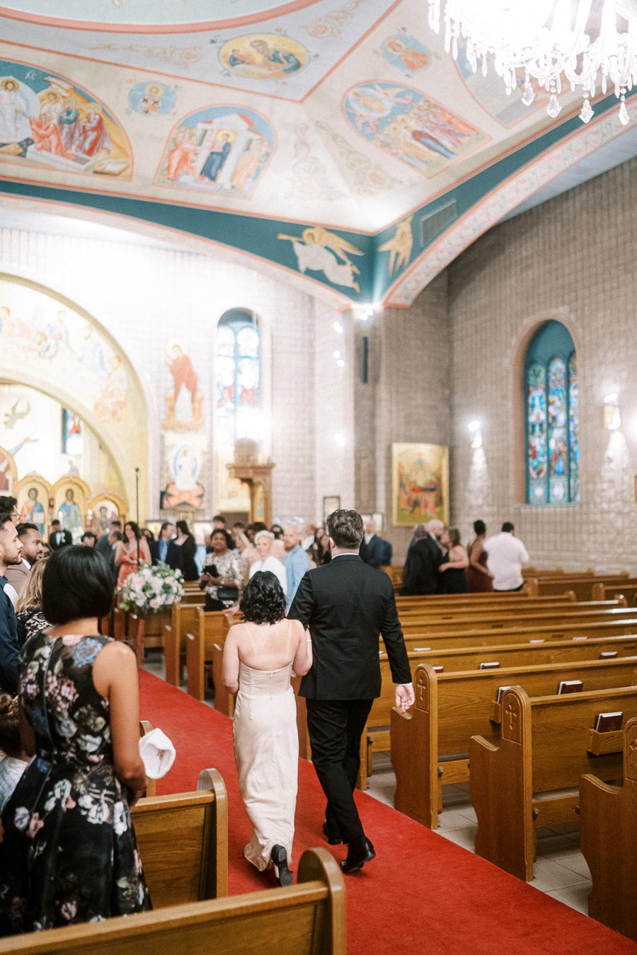 Guests walking down the aisle in a beautifully decorated church with stained glass windows and colorful frescoes on the
