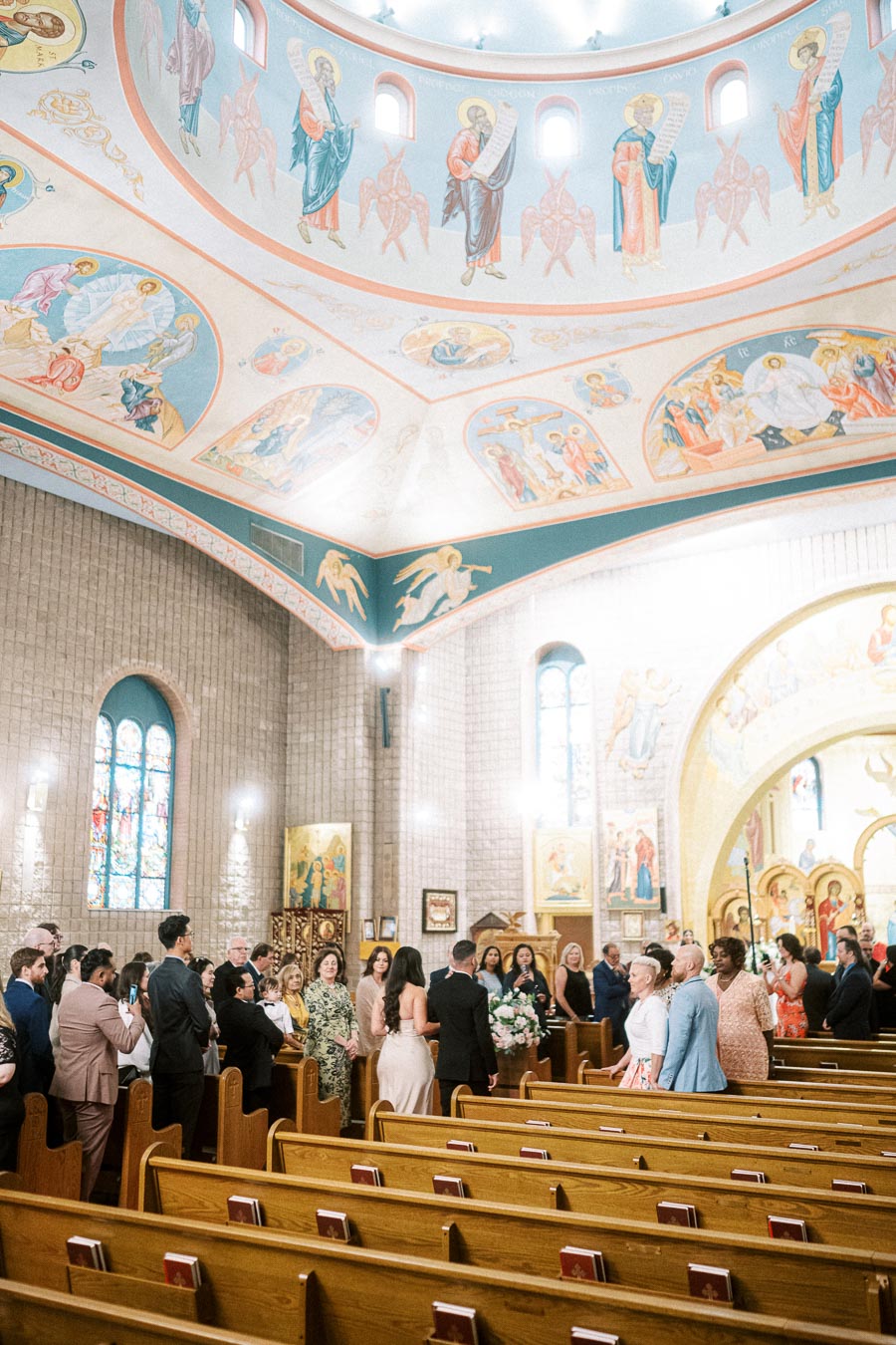 A beautifully decorated church interior filled with people attending a ceremony, featuring ornate ceilings with religious