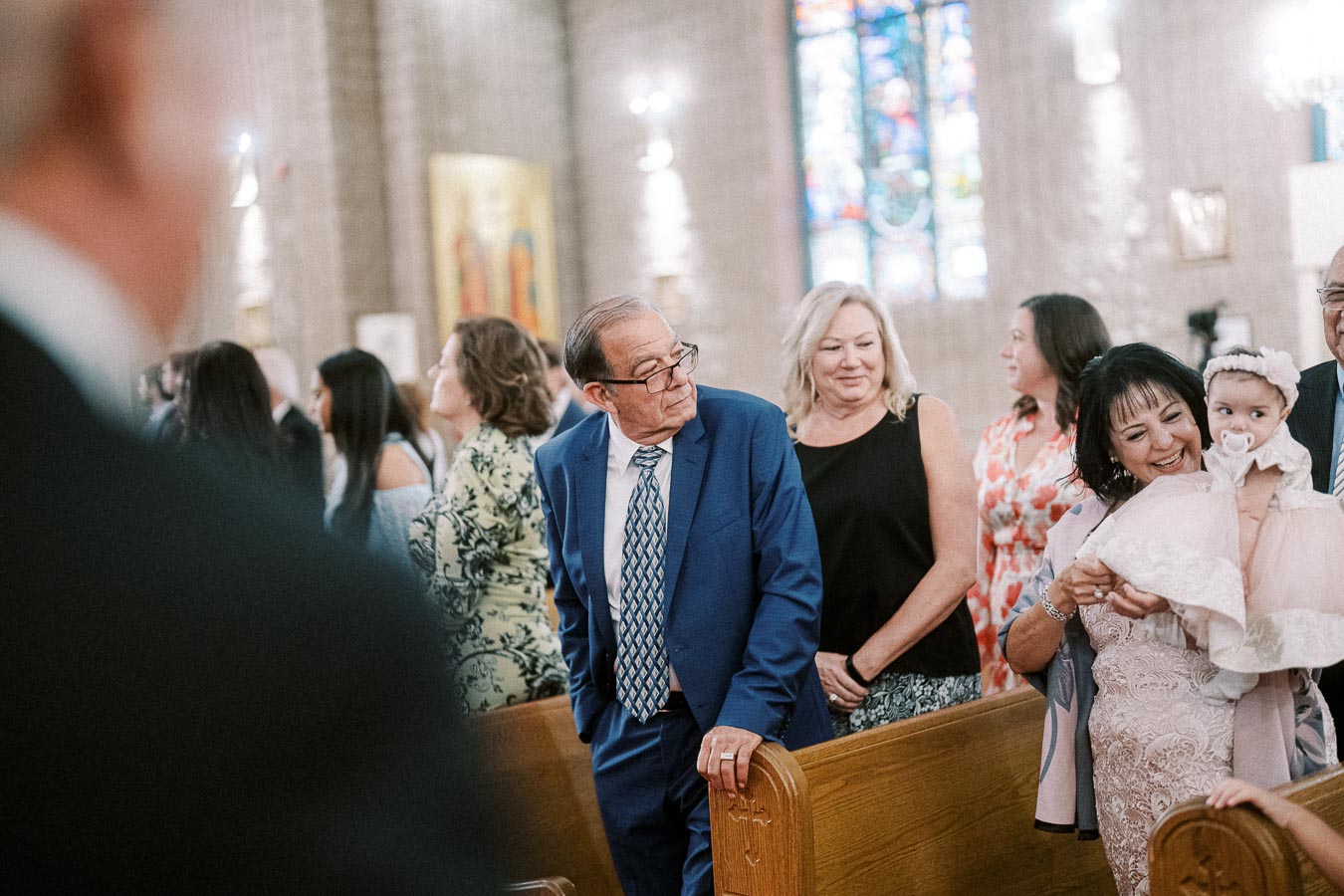 A diverse group of people attending a ceremony inside a church, with stained glass windows in the background, featuring a