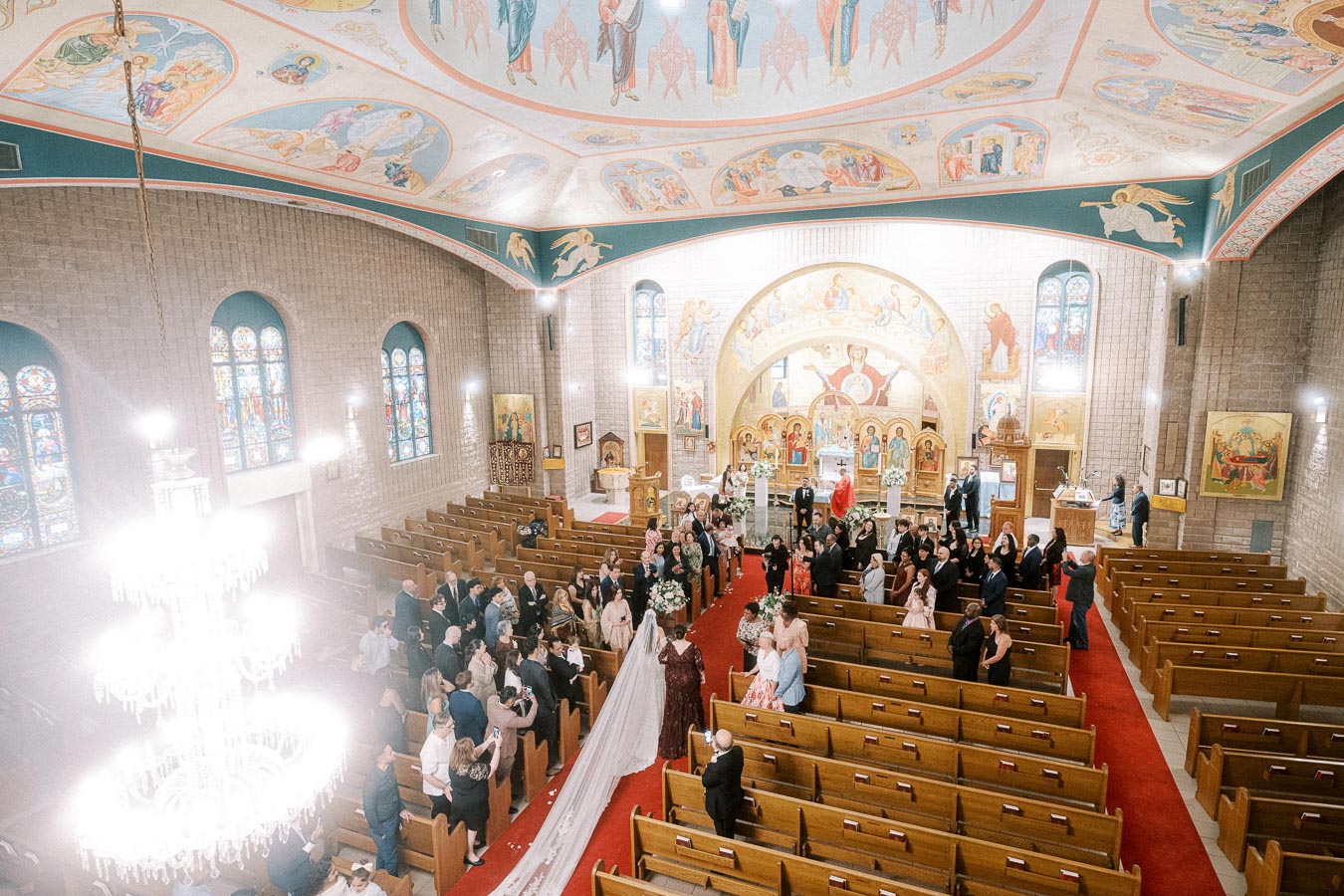 Aerial view of a wedding ceremony in a beautifully decorated church interior with a long bridal train, intricate ceiling