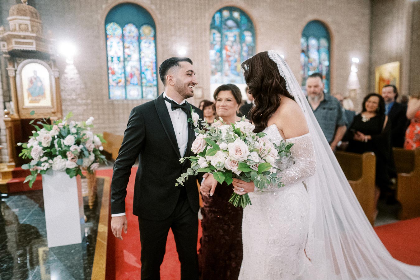 A bride and groom smiling as they walk down the aisle in a church, with the bride holding a bouquet of white and pink