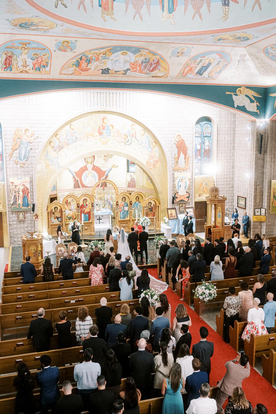 Wedding ceremony in an ornate church with a decorated ceiling, featuring a bride and groom at the altar surrounded by guests
