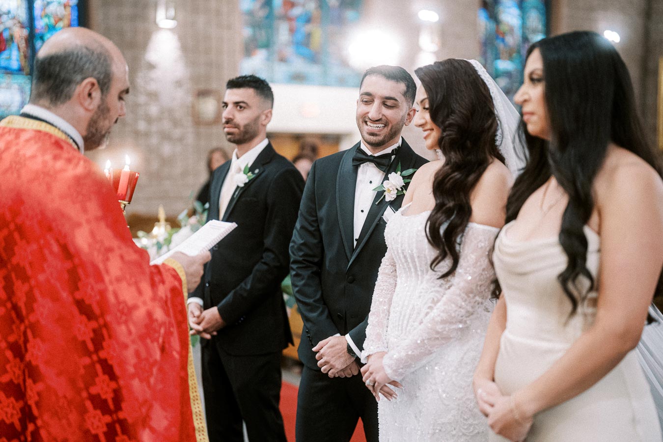 A wedding ceremony in a church with a couple in formal attire, accompanied by a bridesmaid and groomsman, as an officiant in