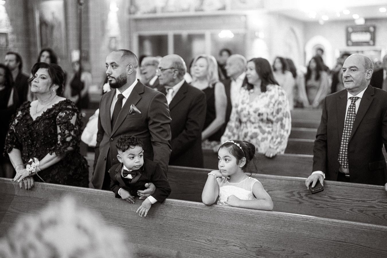 A black and white photo of people attending a formal ceremony in a church, including a man in a suit with a child by his