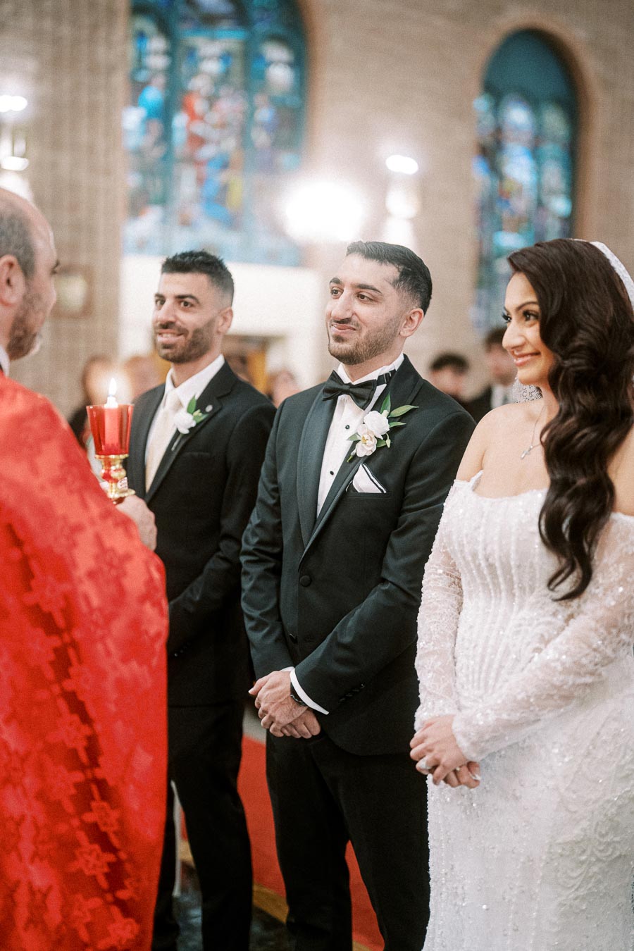 A bride and groom smiling during a traditional wedding ceremony inside a church, with stained glass windows in the