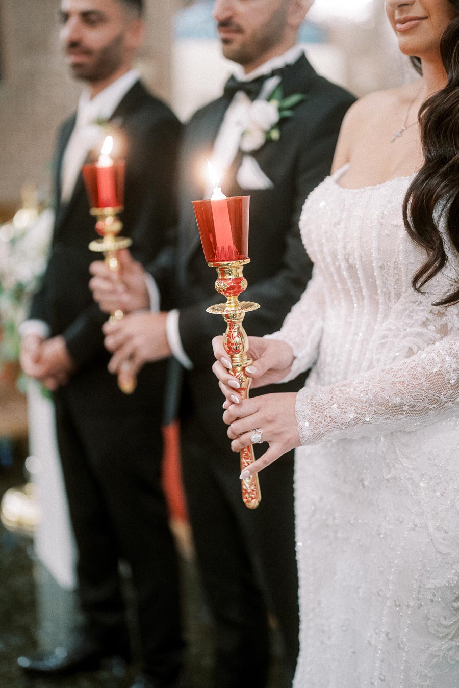 People in elegant attire holding ornate candles at a formal event or ceremony, featuring intricate candle holders and a