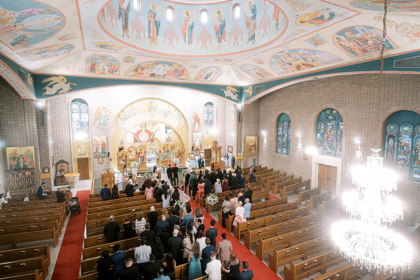 Aerial view of an ornate church interior with iconic frescoes and stained glass windows, featuring a congregation attending