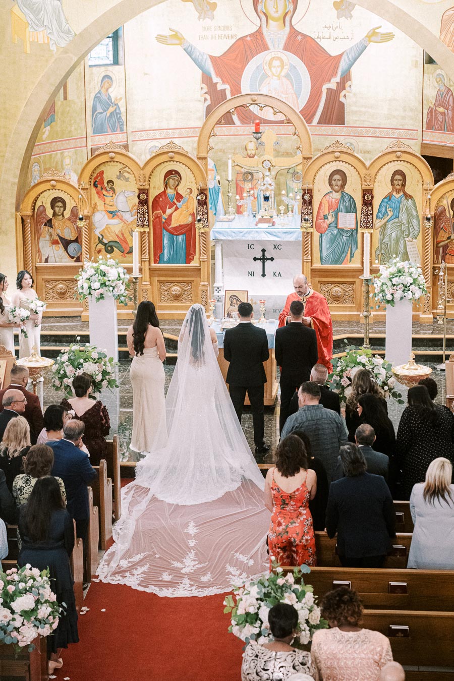 A traditional wedding ceremony inside an ornate church with religious icons on the walls, featuring a bride in a long white