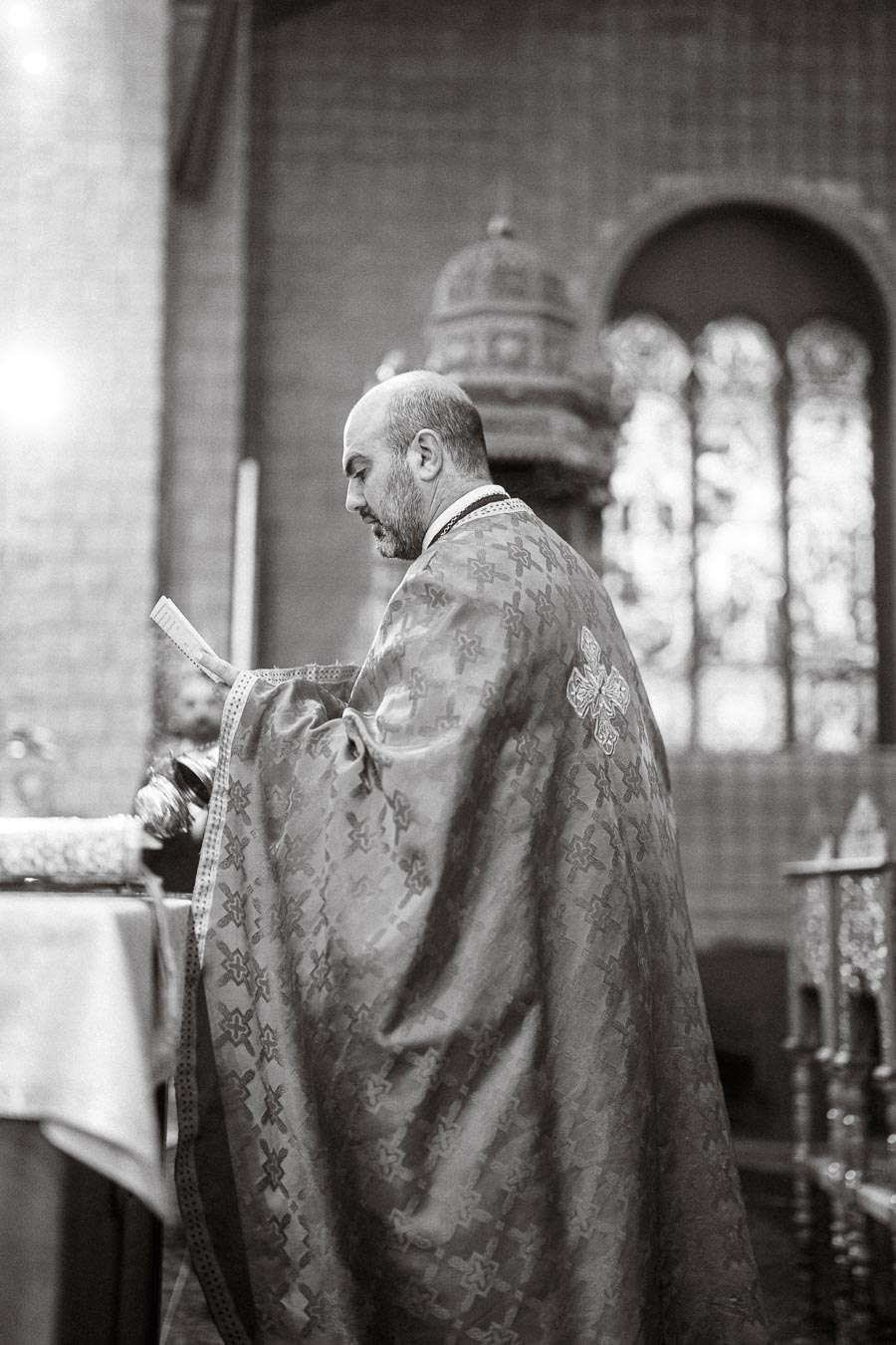 Priest conducting a religious ceremony in a church, wearing ornate vestments, with an intricately designed stained