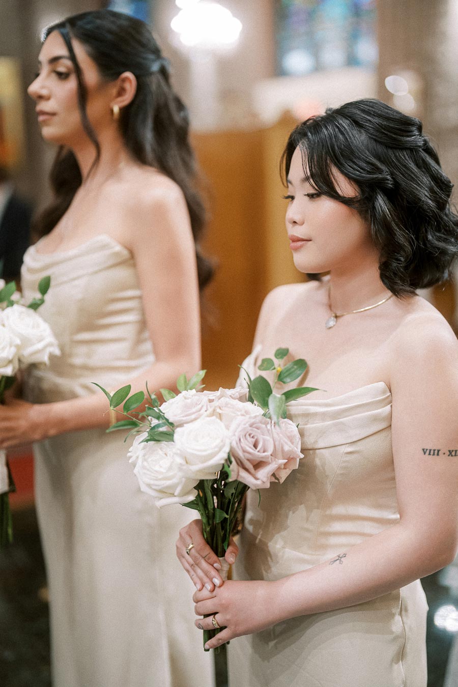 Bridesmaids in elegant cream dresses holding bouquets of white and blush roses during a wedding ceremony.