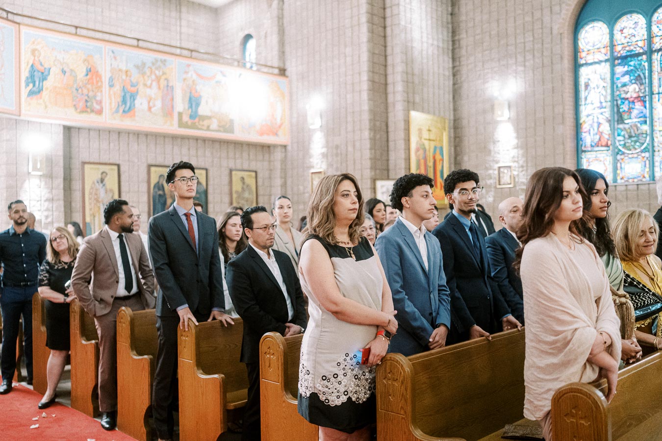 A diverse group of people attending a formal event in a church, standing in wooden pews, surrounded by religious artwork and