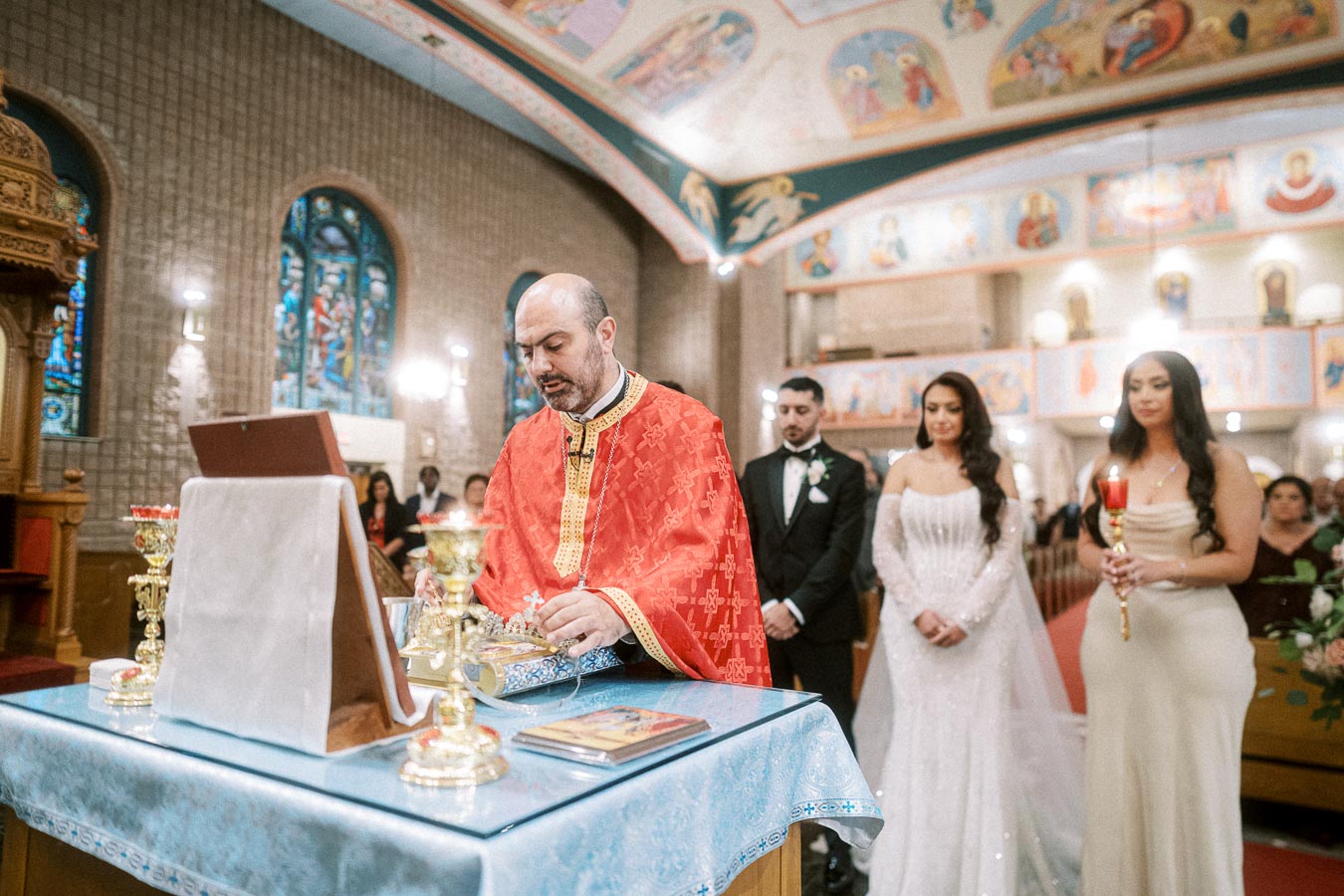 A priest in red vestments conducts a traditional wedding ceremony at a beautifully decorated church, with a couple standing