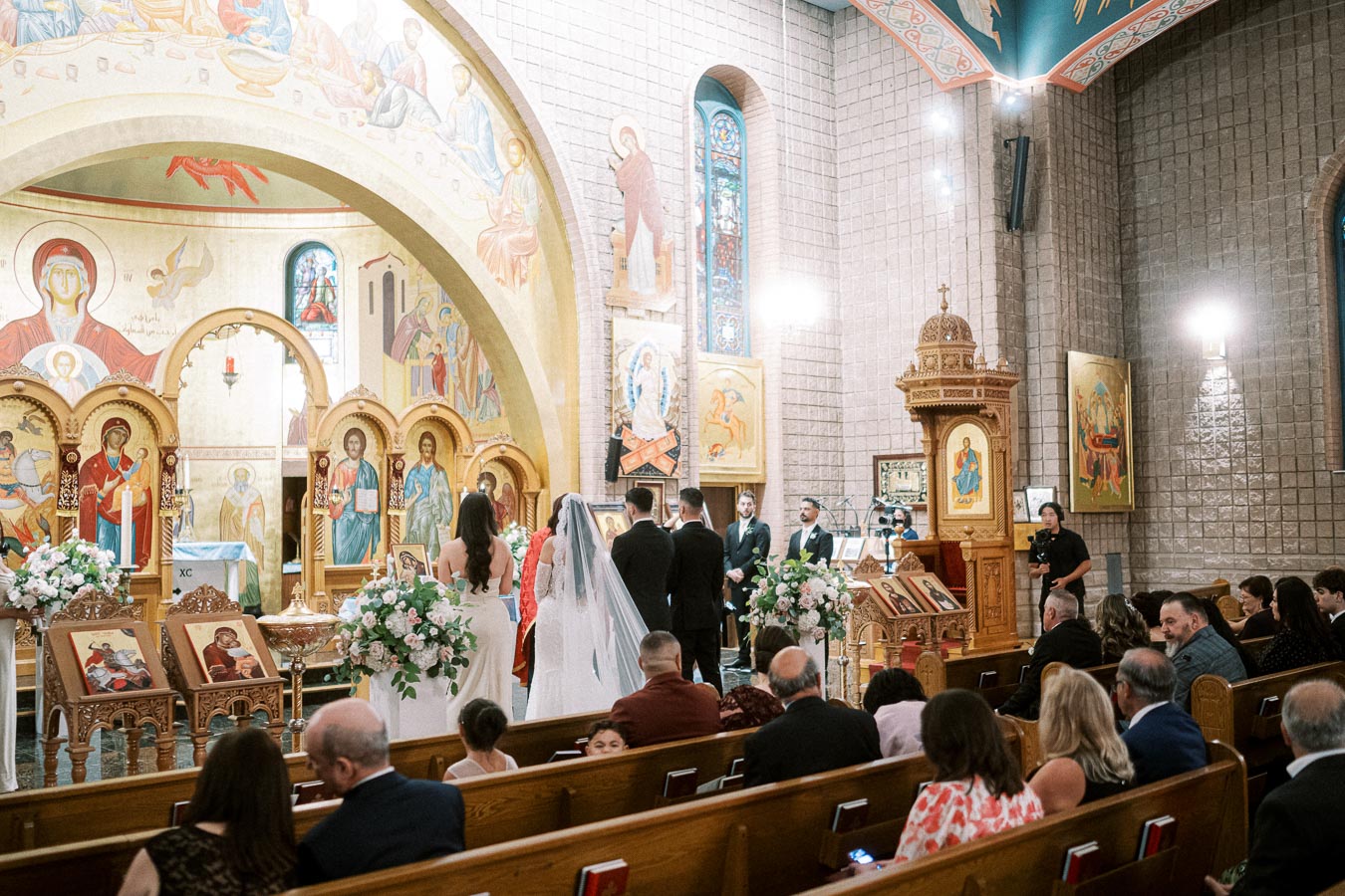 Greek Orthodox wedding ceremony in a beautifully decorated church, featuring vibrant religious icons and floral