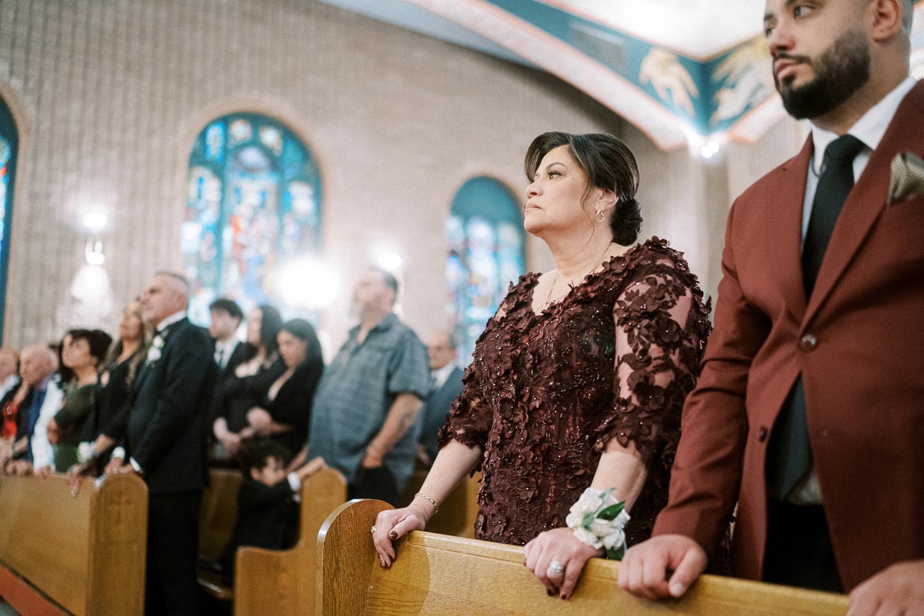 A group of people standing in a church during a ceremony, with stained glass windows in the background.