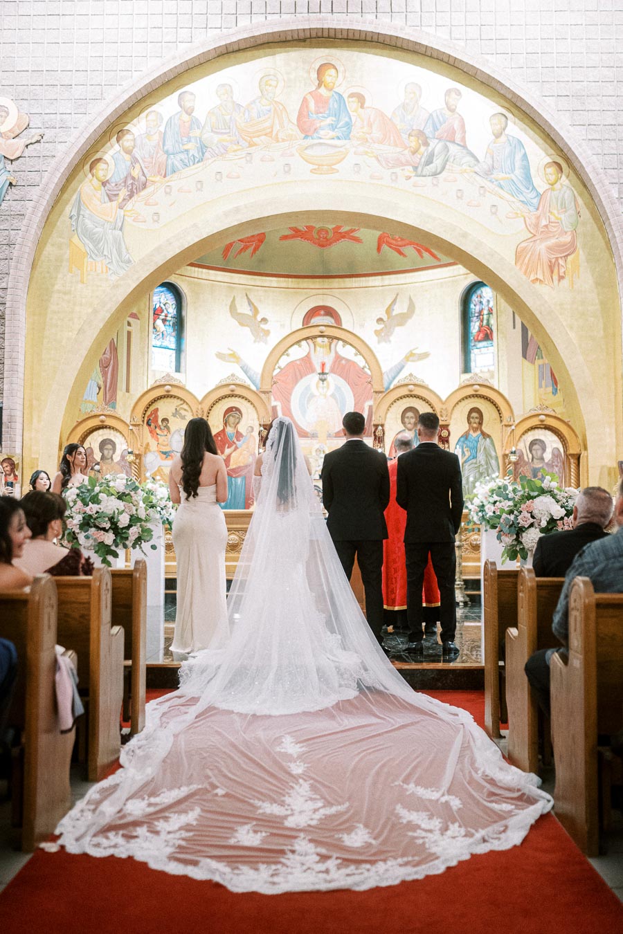 Wedding ceremony inside a church, featuring a bride in a long, lace-embroidered gown and veil, standing with a groom in a