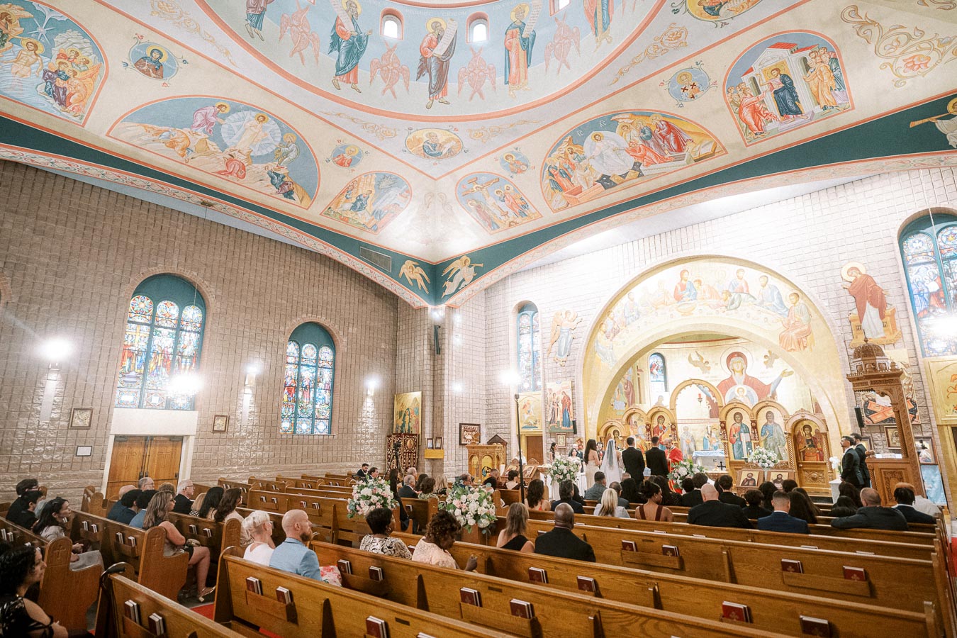 Interior of an ornately decorated church during a wedding ceremony, featuring colorful frescoes on the ceiling, vibrant
