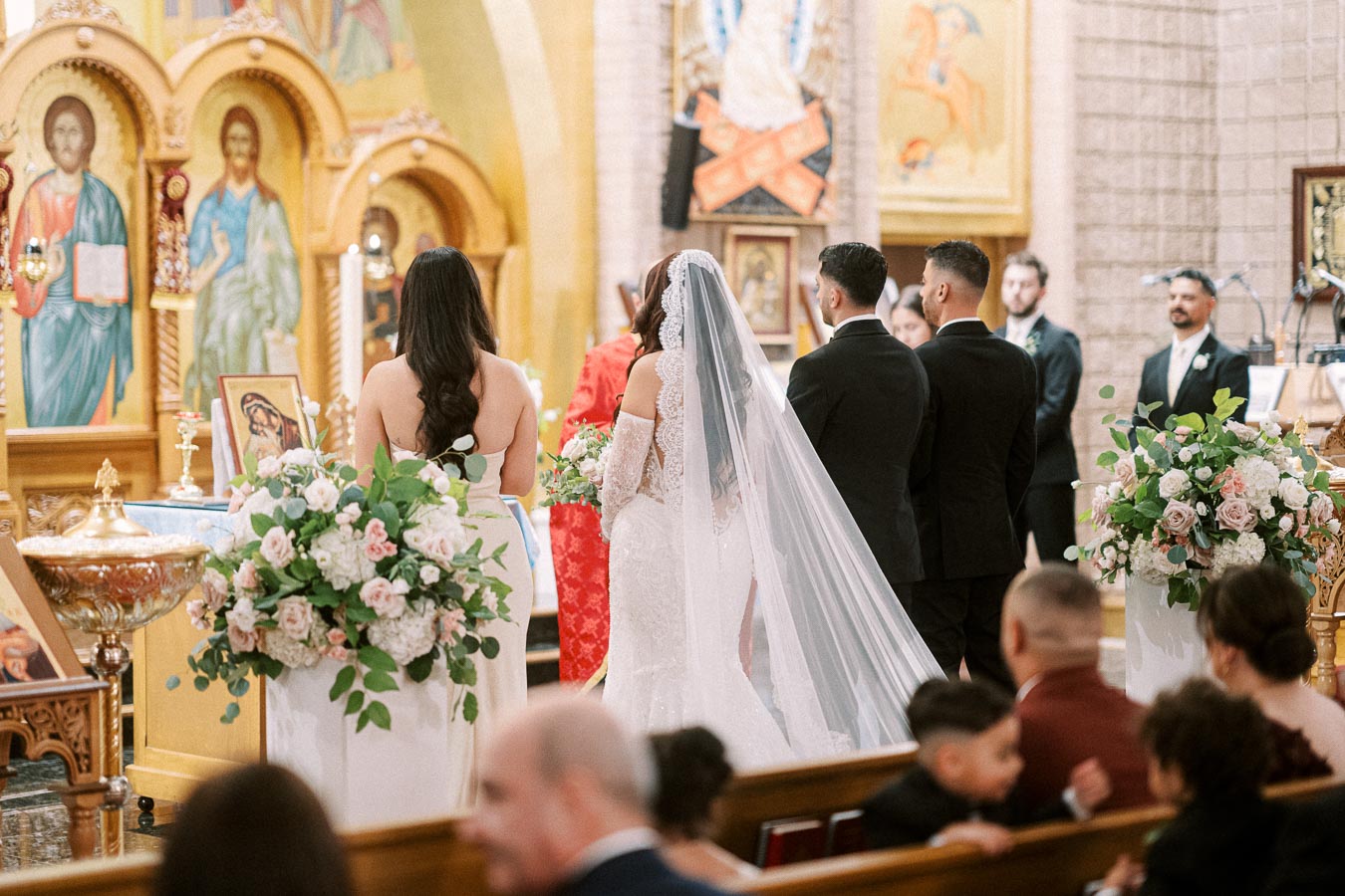 A bride in a white lace gown with a long veil stands at the altar beside the groom during a traditional church wedding