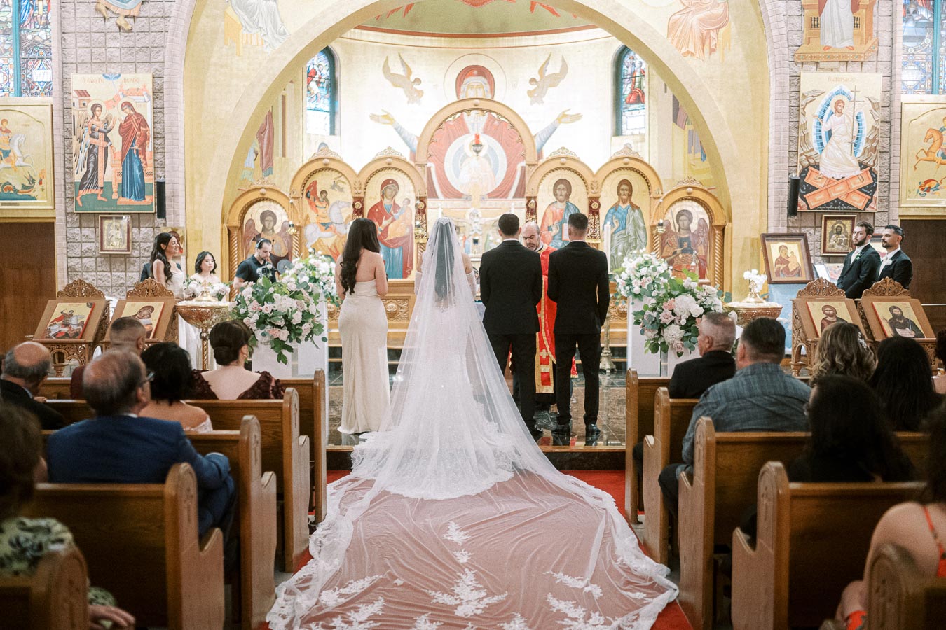 Orthodox wedding ceremony taking place in a richly decorated church, featuring a bride in a long, flowing veil and groom