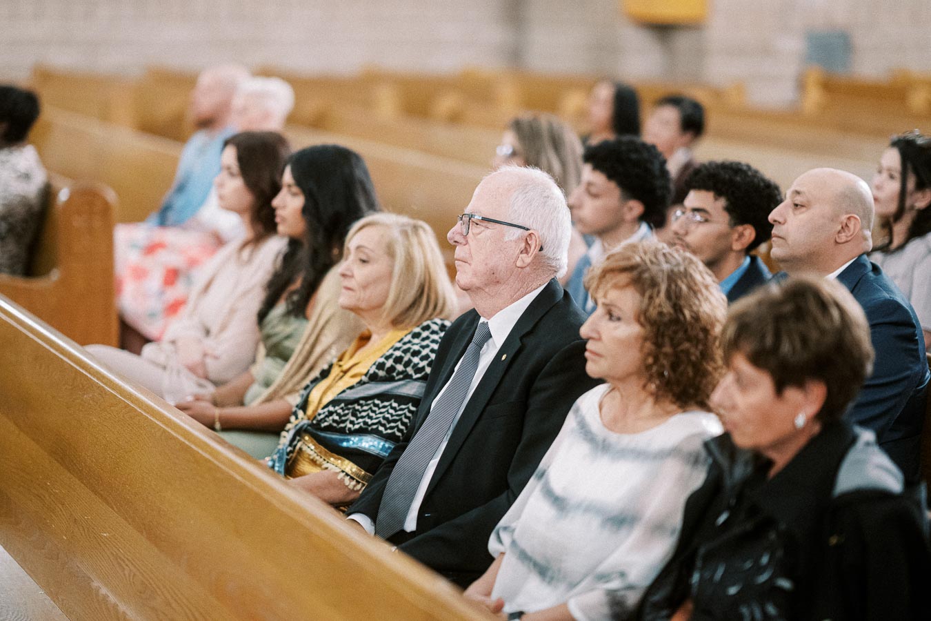 A diverse group of people seated in wooden church pews attentively listening during a service.