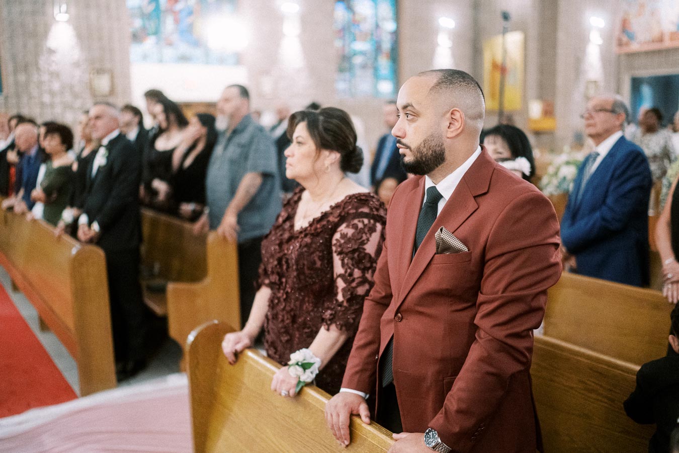 A congregation attending a formal event inside a church, with a man in a red suit and a woman in a decorative maroon dress