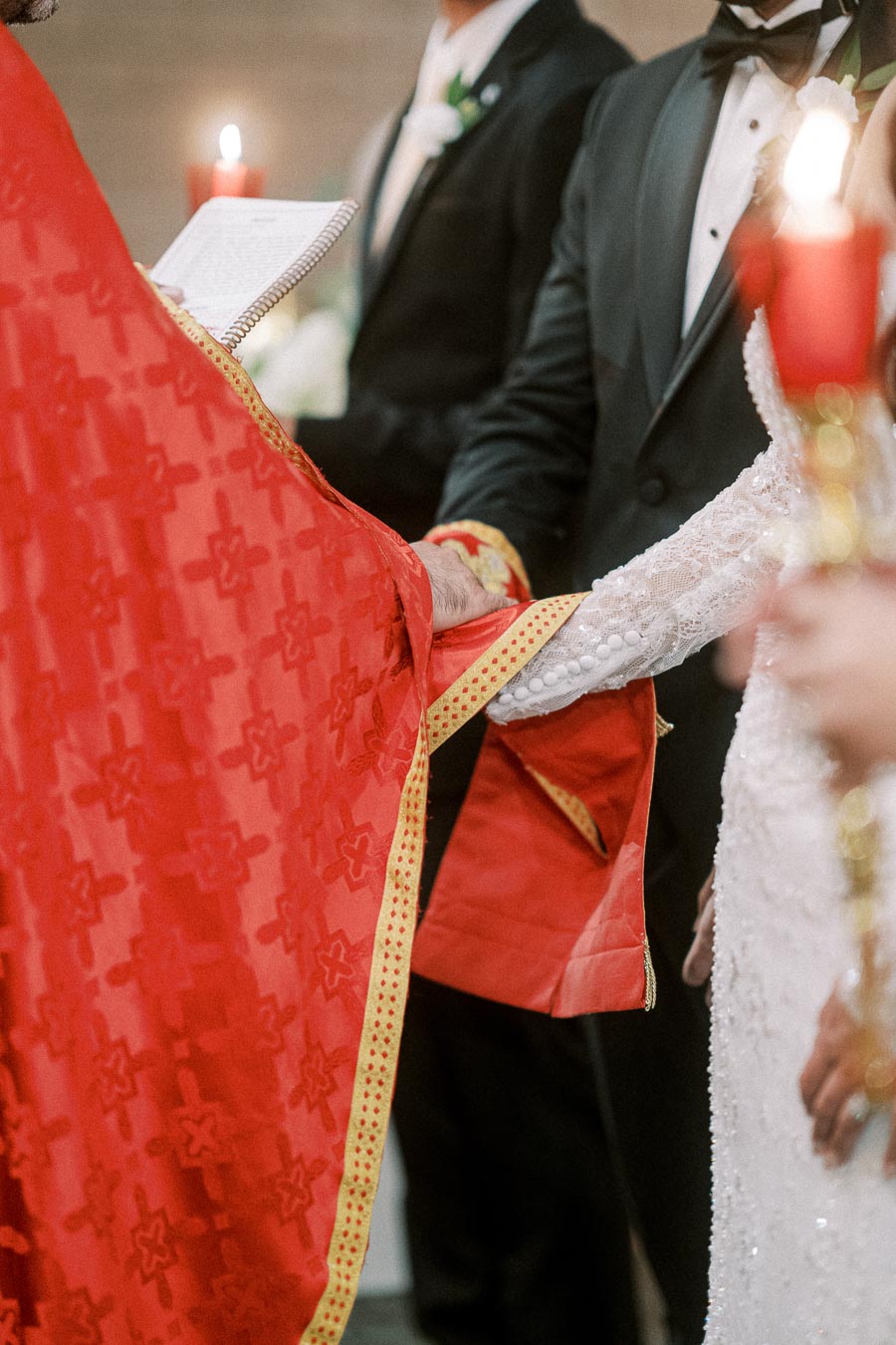 A priest in a red robe holding hands with a bride and groom during a traditional wedding ceremony, with a focus on the