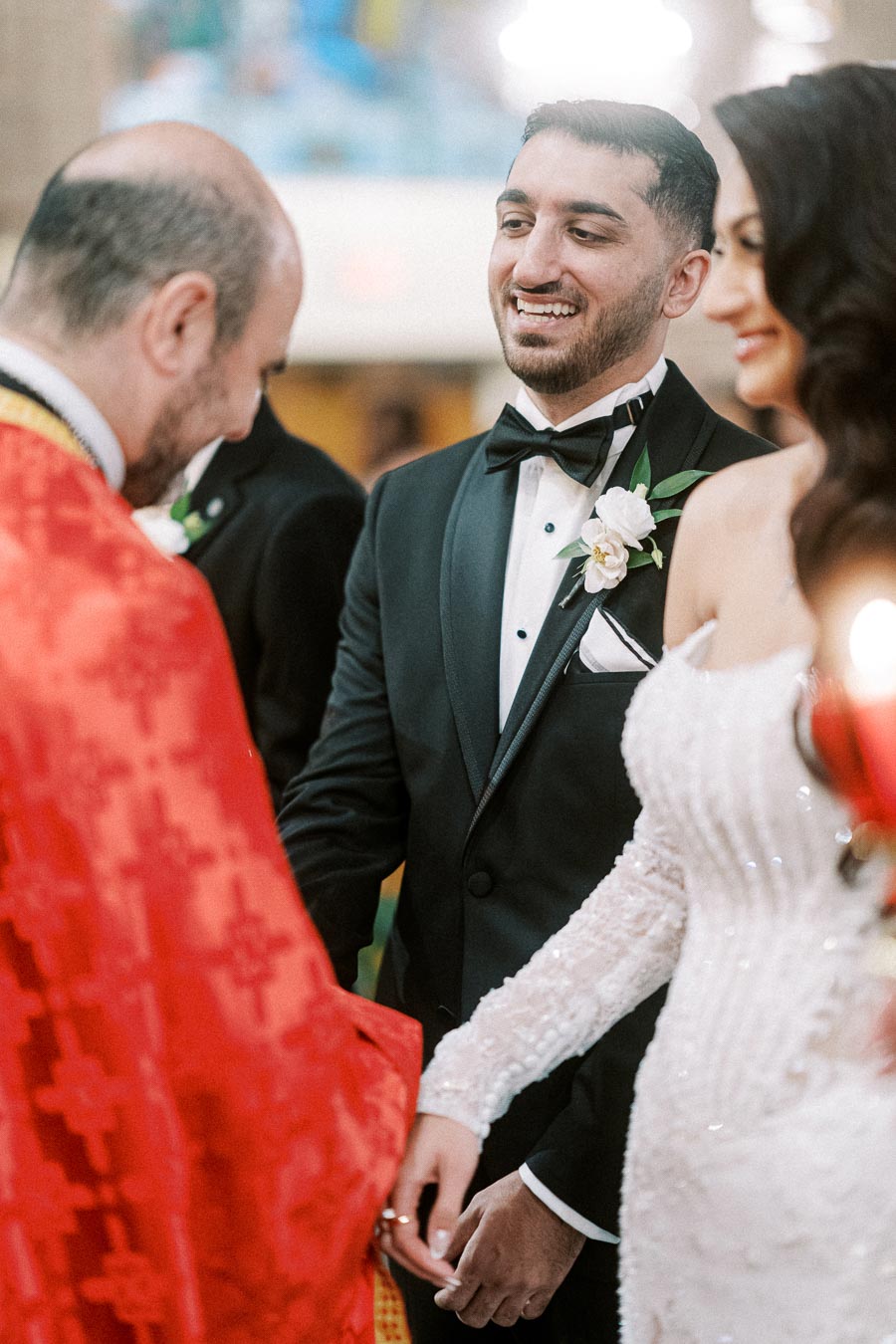 Wedding ceremony with a smiling groom in a black tuxedo and bride in a white gown while holding hands, officiated by a
