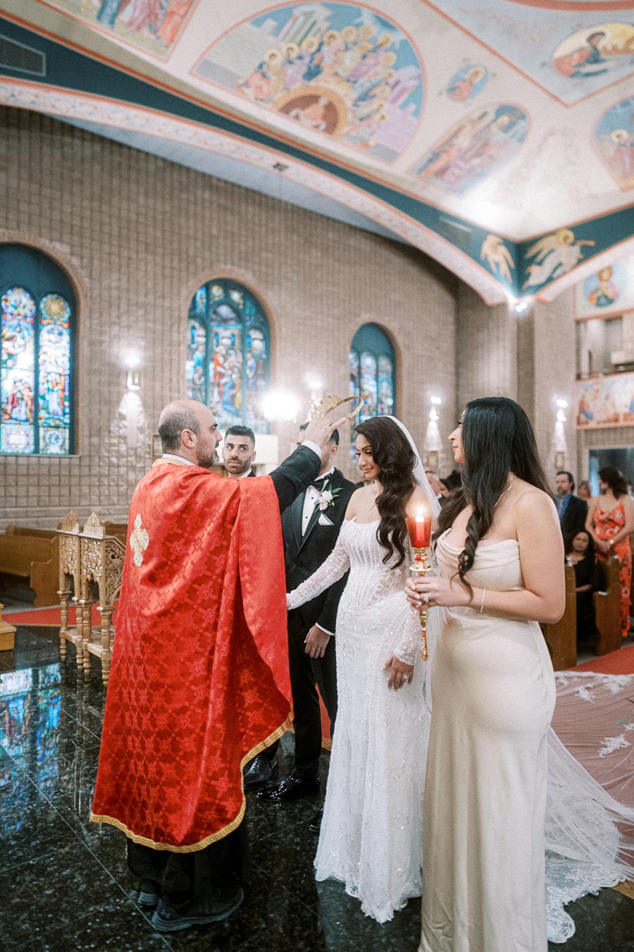 Priest performing a traditional wedding ceremony, placing a crown on the bride's head in an ornate church with stained glass
