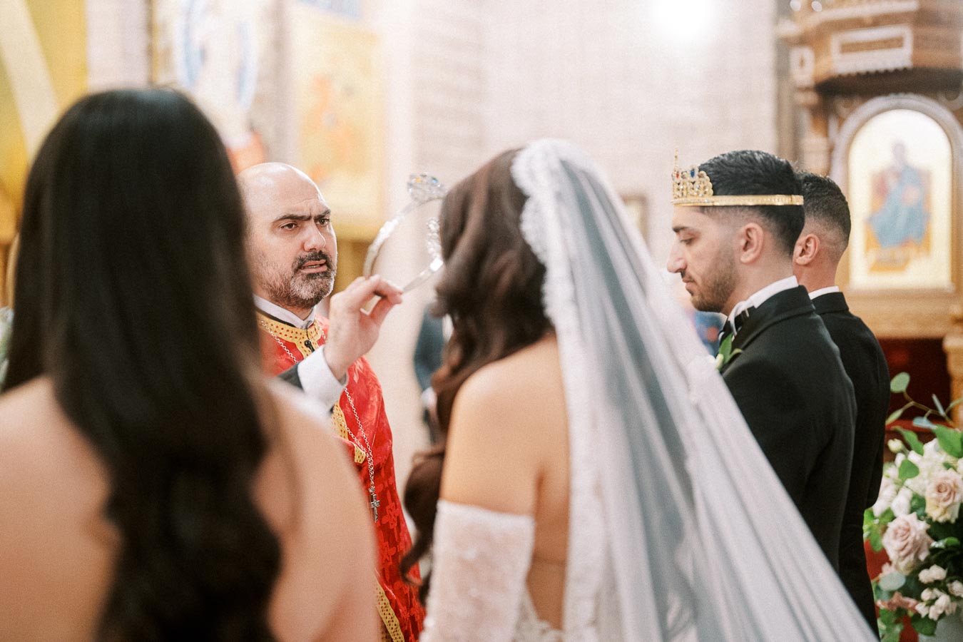 A religious wedding ceremony taking place in a church, featuring a priest wearing a red robe performing a ritual with a