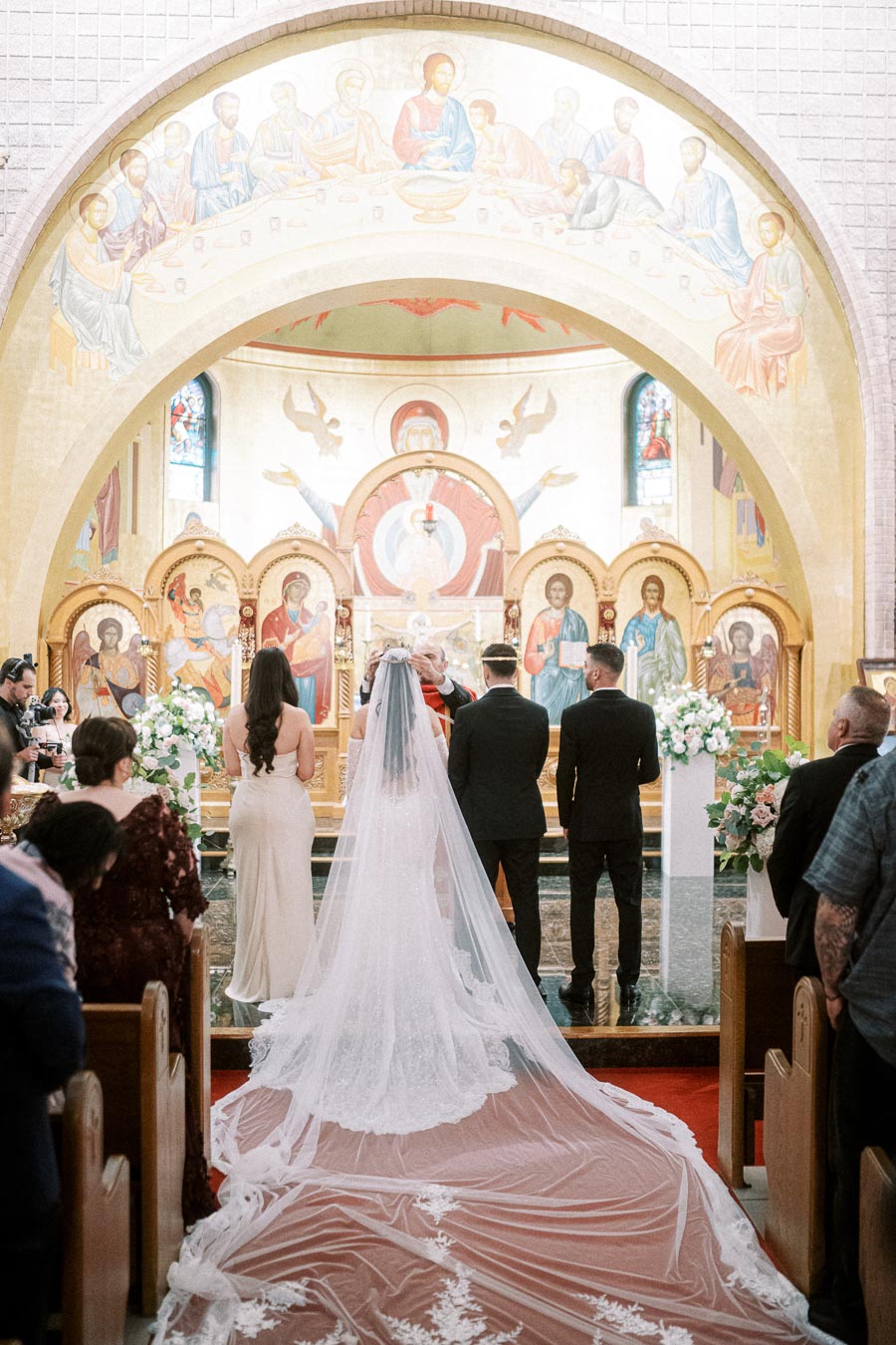 A bride and groom stand at the altar during a wedding ceremony in an ornate church, surrounded by guests and religious