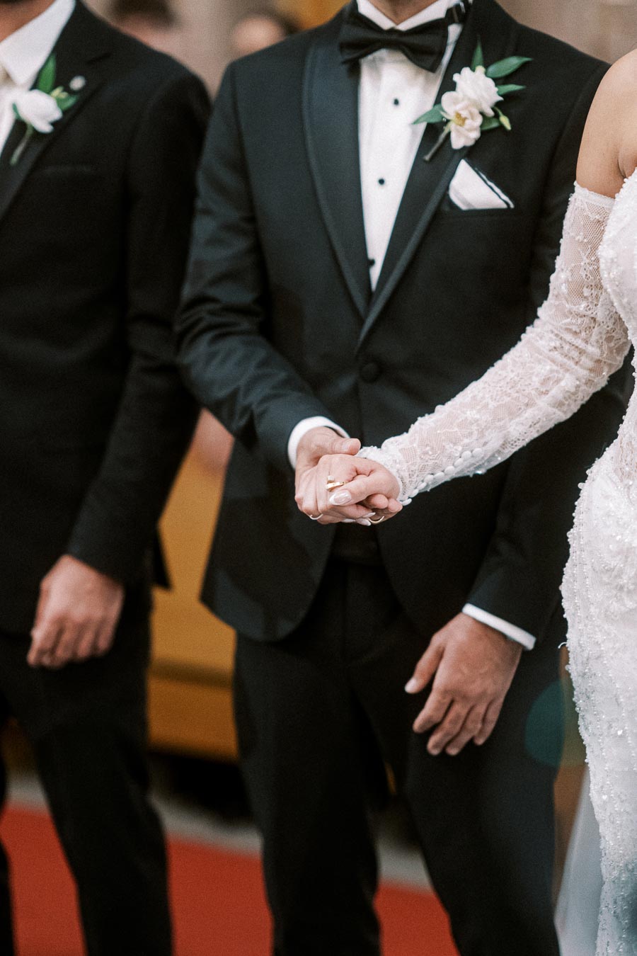 Couple holding hands during wedding ceremony, groom in black tuxedo and bride in lace wedding dress, symbolizing love and