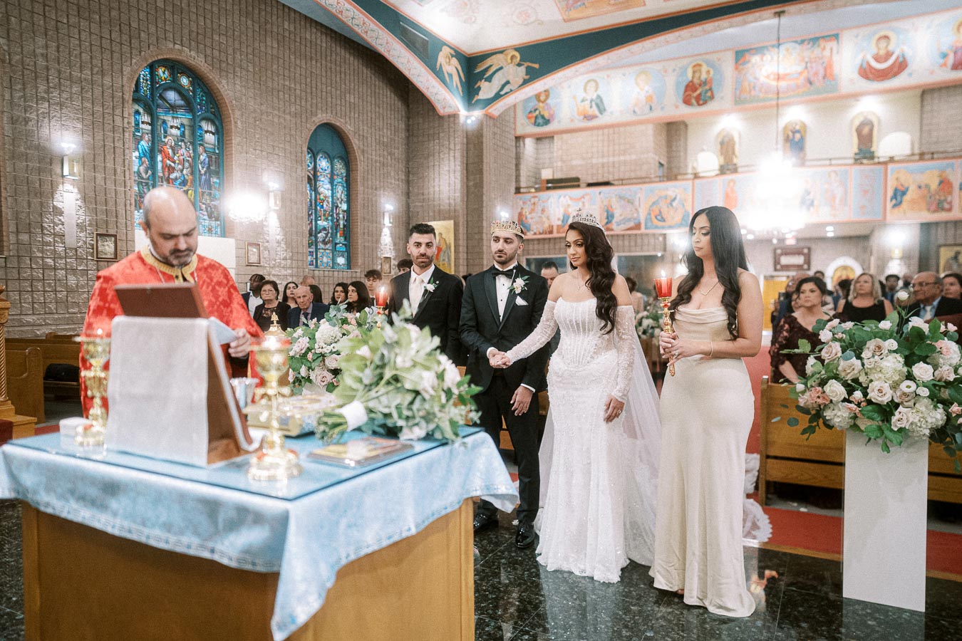 Orthodox wedding ceremony inside a beautifully decorated church, featuring a couple standing before a priest. The bride is