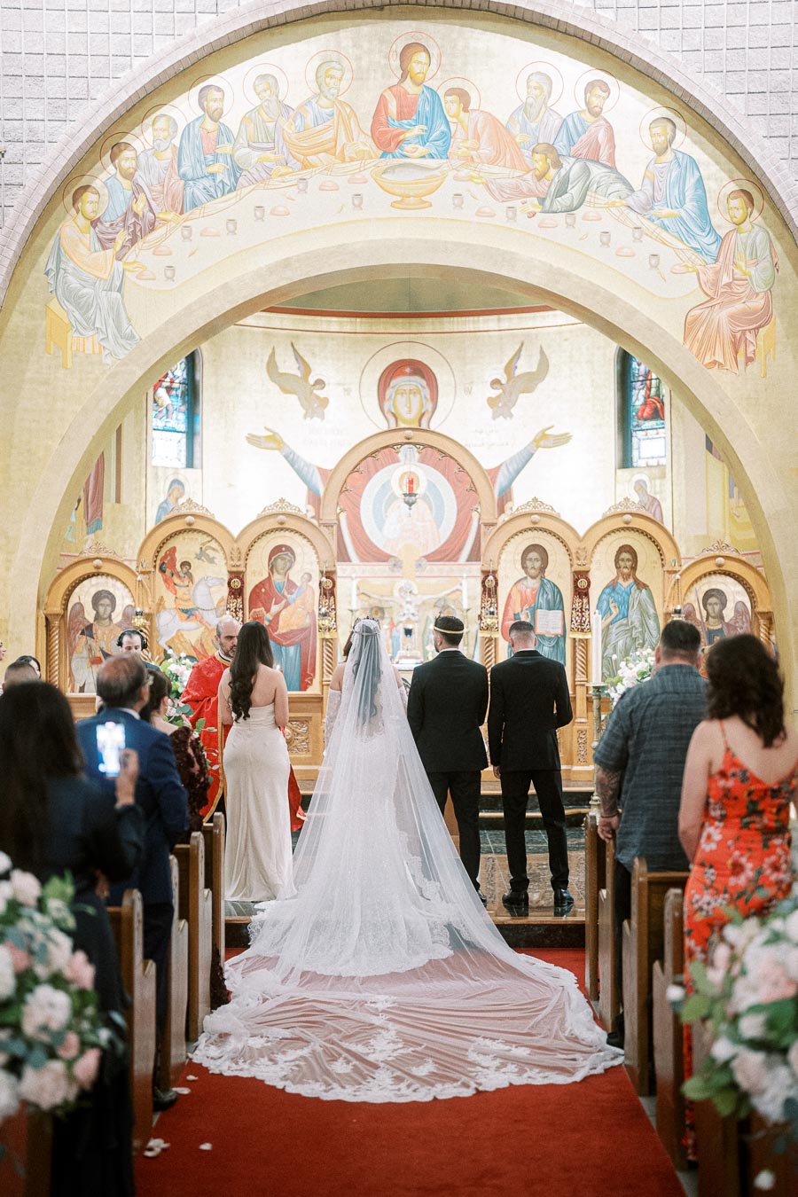 A bride in an elegant white gown with a long train stands at the altar with the groom in a church adorned with religious
