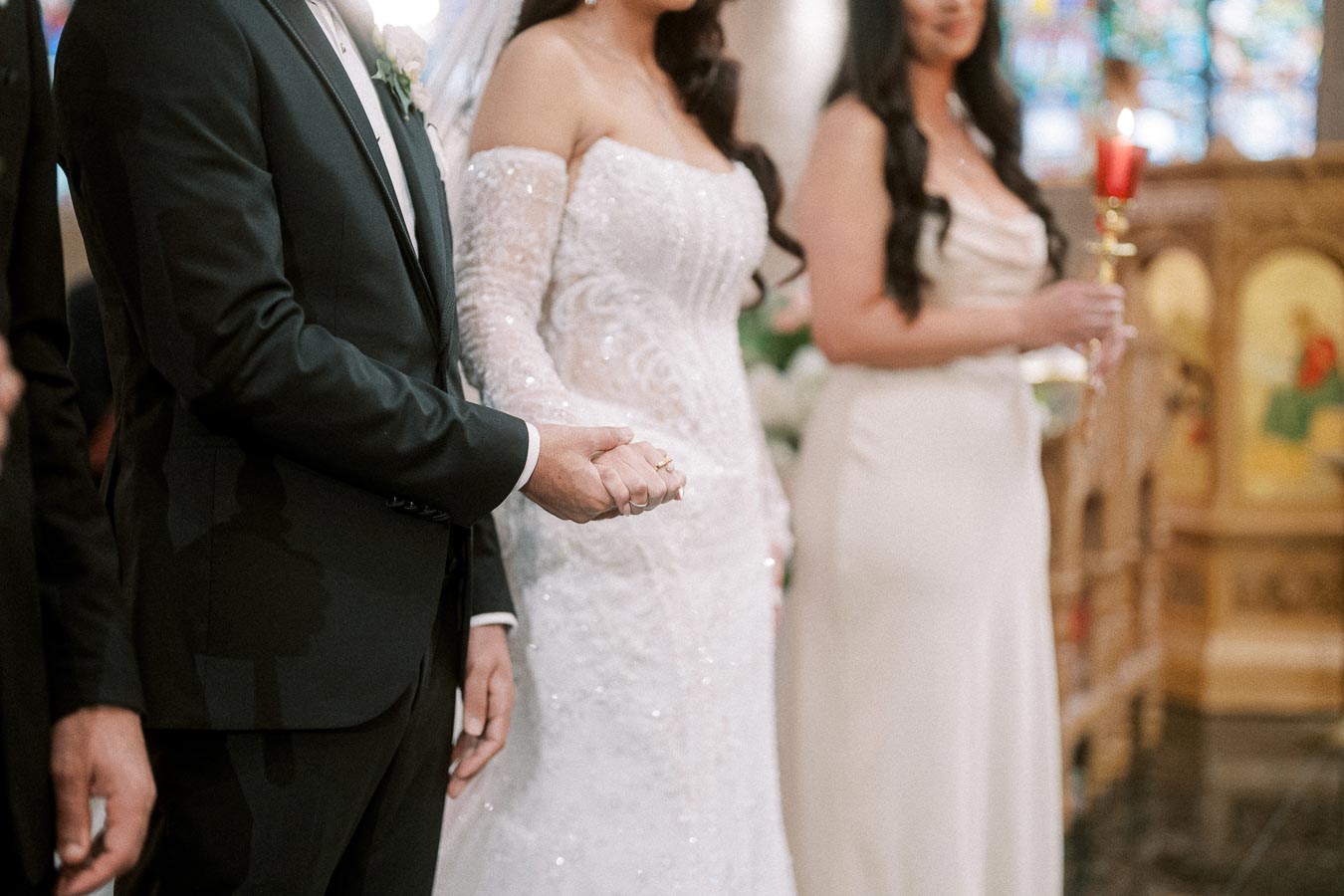 A bride and groom holding hands at a wedding ceremony, with the bride in a white lace gown and the groom in a black suit,