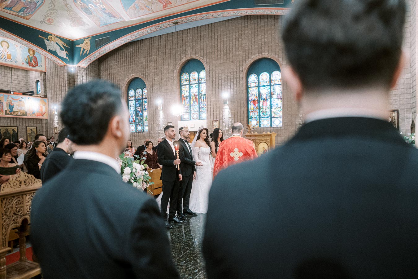 A bride and groom stand together during a traditional wedding ceremony in a beautifully decorated church with stained glass