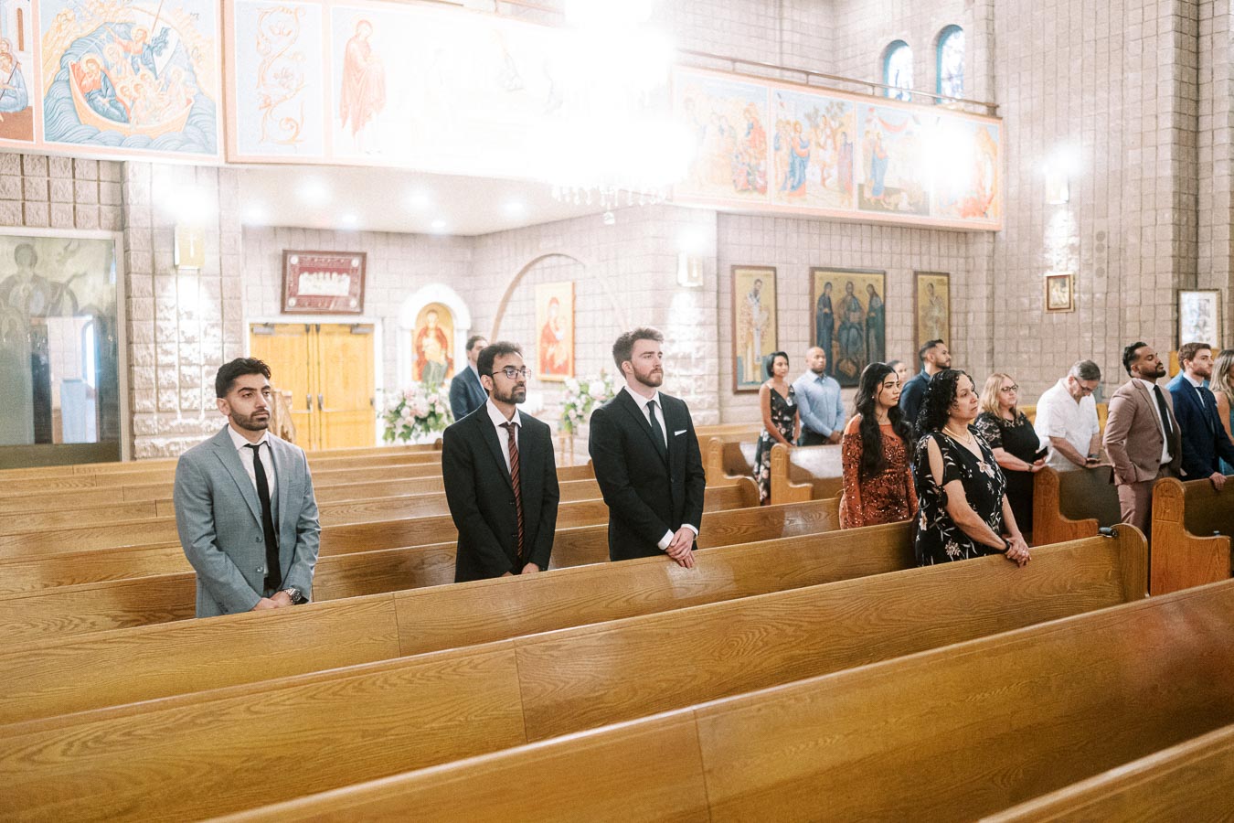 A group of people standing in the pews of a beautifully decorated church, attending a formal event or ceremony. The church