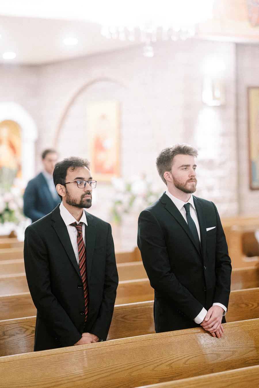 Two men in suits standing in a church during a formal event, surrounded by wooden pews and soft lighting.