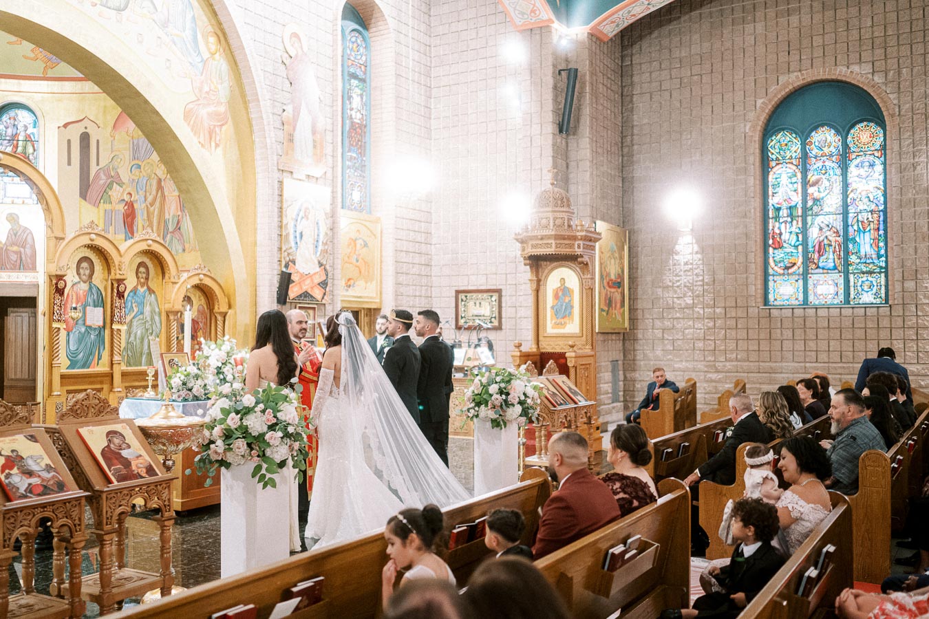 A bride and groom stand before a priest during a traditional wedding ceremony in a beautifully adorned church, featuring