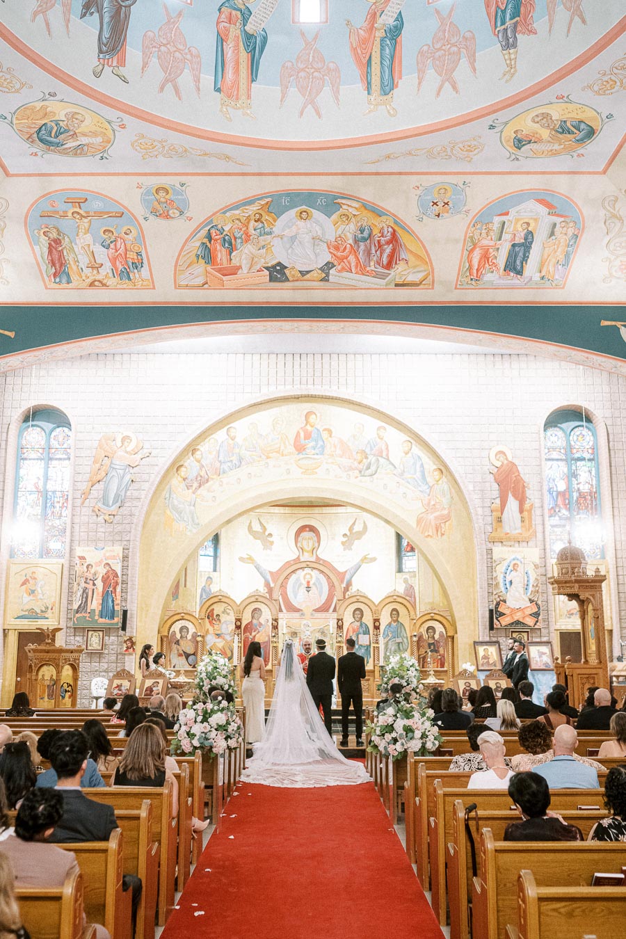 A couple exchanging vows in a beautifully decorated Orthodox church, featuring vibrant religious icons, floral arrangements,