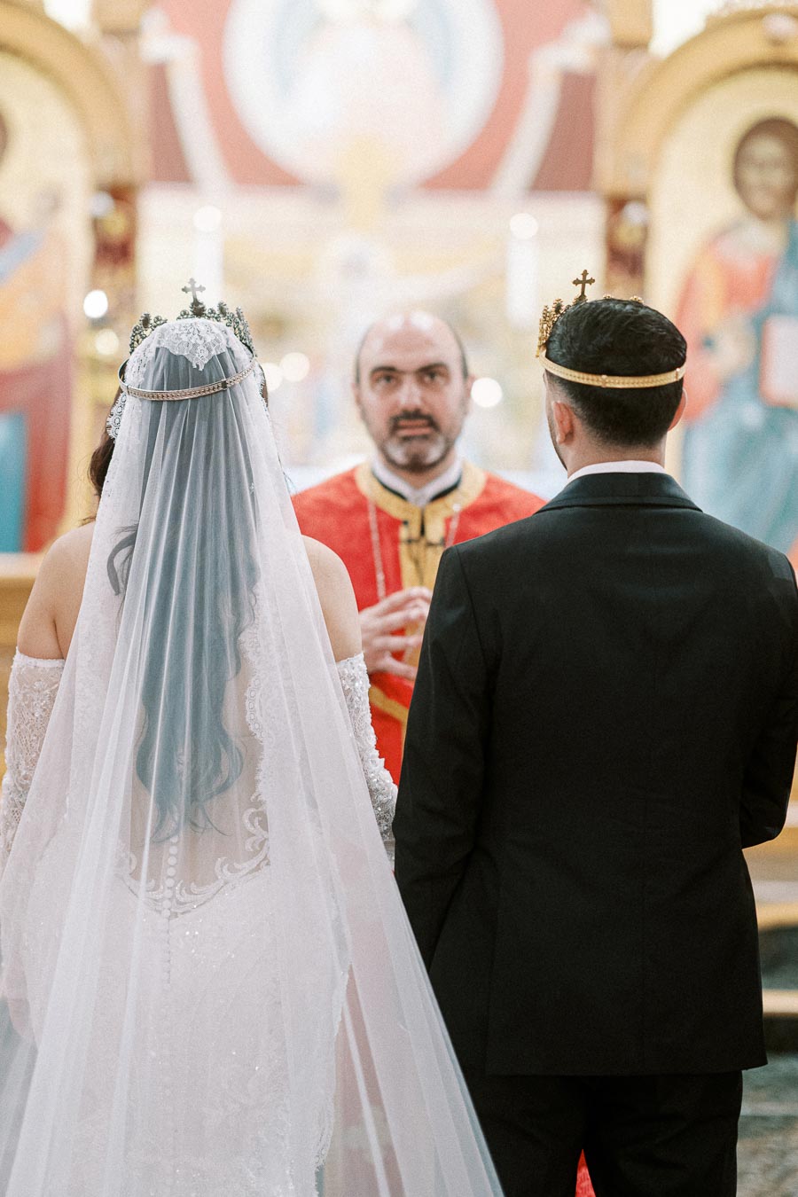 A bride and groom wearing traditional crowns during a wedding ceremony in an ornate church setting.