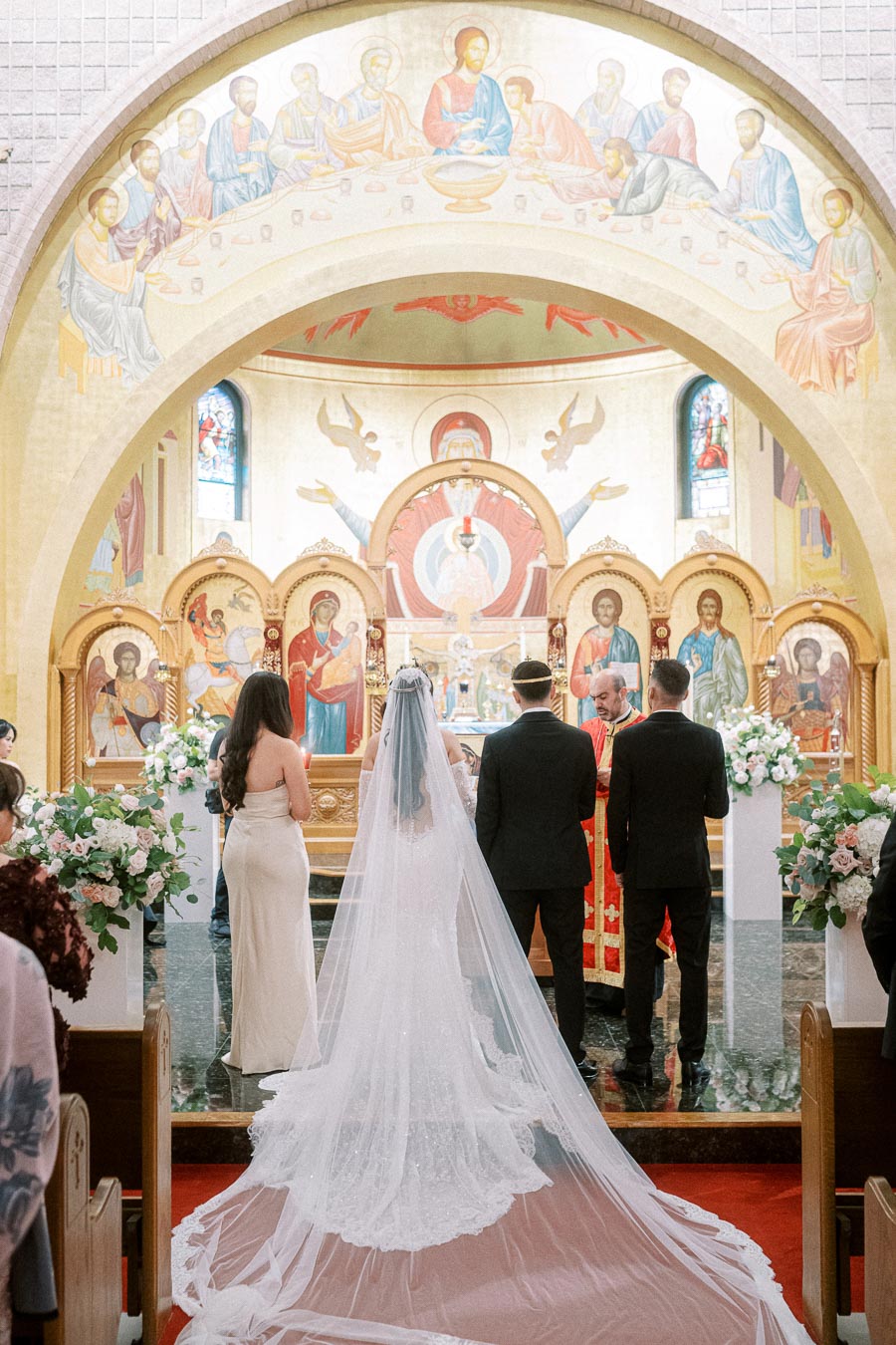 A bride and groom stand at the altar in a beautifully decorated church, surrounded by intricate religious icons and