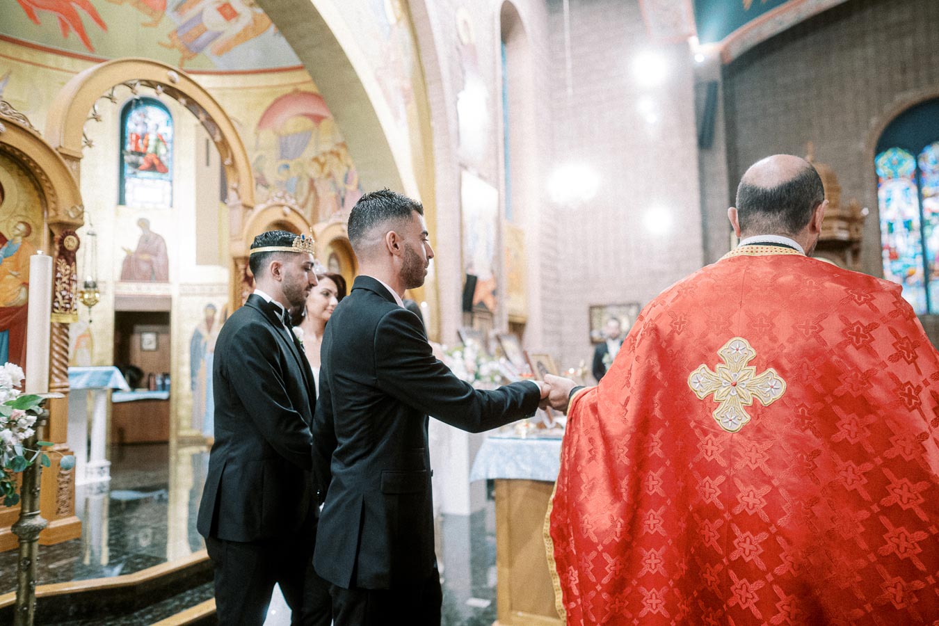 Orthodox wedding ceremony inside a beautifully decorated church, featuring a priest in traditional red vestments