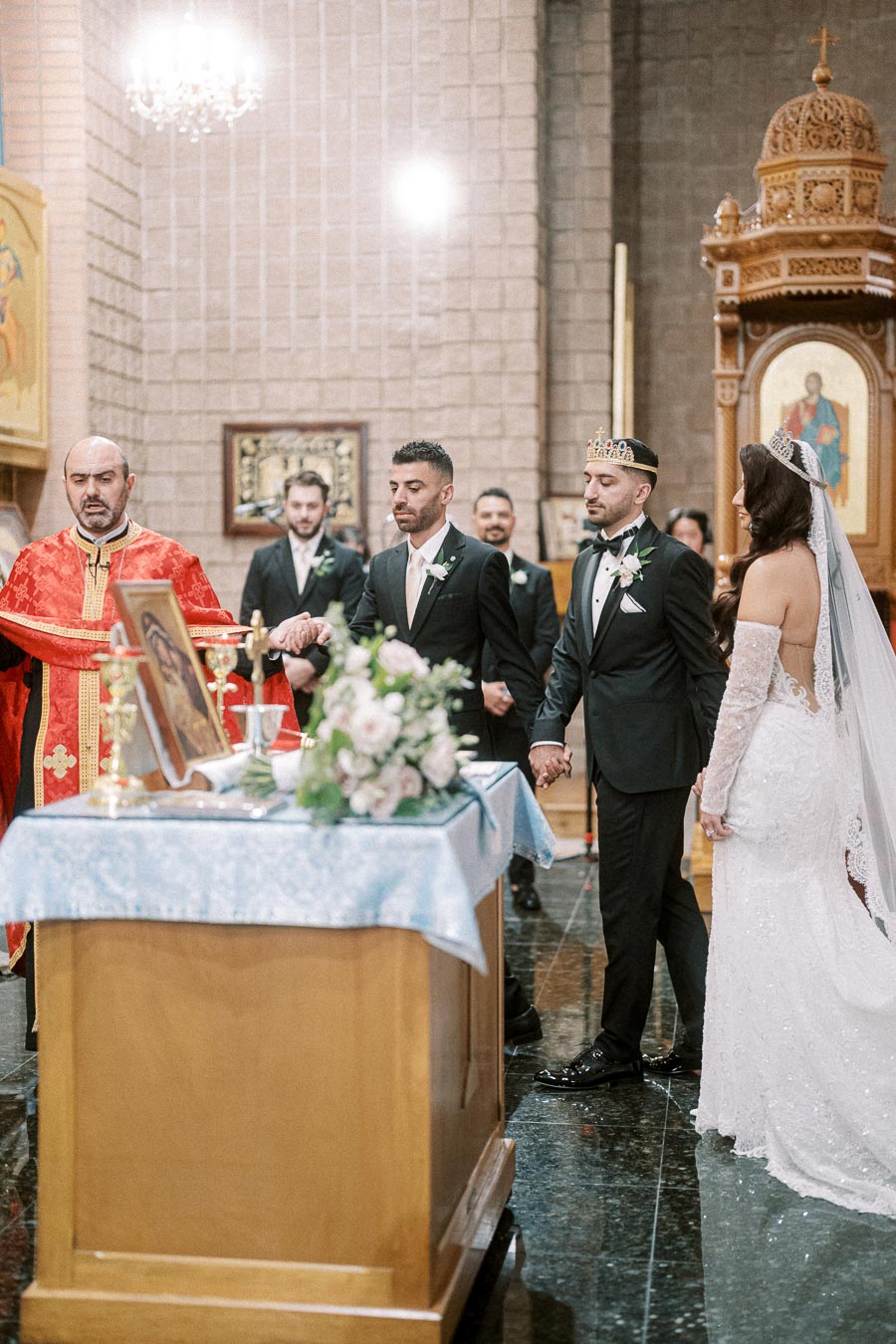 Orthodox wedding ceremony in a church, featuring a bride in a white gown and groom in a black tuxedo with crowns, standing