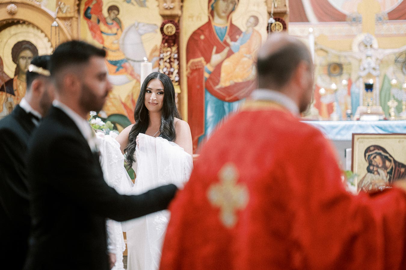 A bride and groom participate in a traditional religious wedding ceremony inside an ornately decorated church, featuring