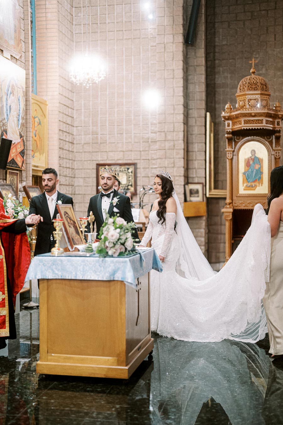 A bride and groom stand before an altar during a traditional church wedding ceremony, adorned with crowns, surrounded by