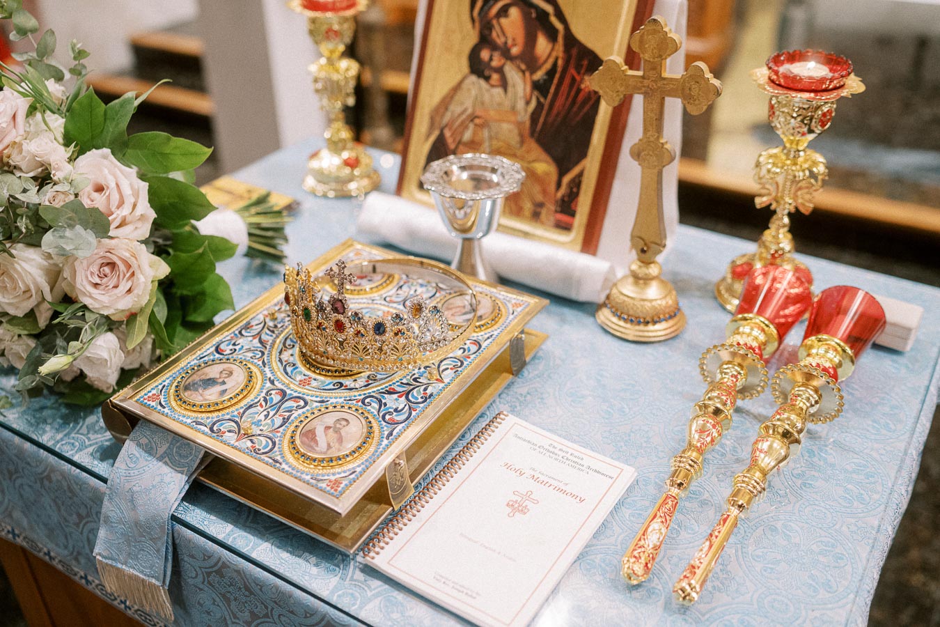 Orthodox wedding ceremony table with floral arrangement, ornate gold crown on an embellished book, religious