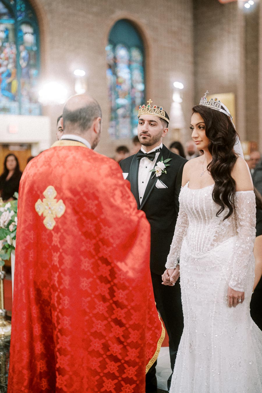 Wedding ceremony in a church with a couple wearing crowns holding hands, dressed in a suit and an elegant white gown,
