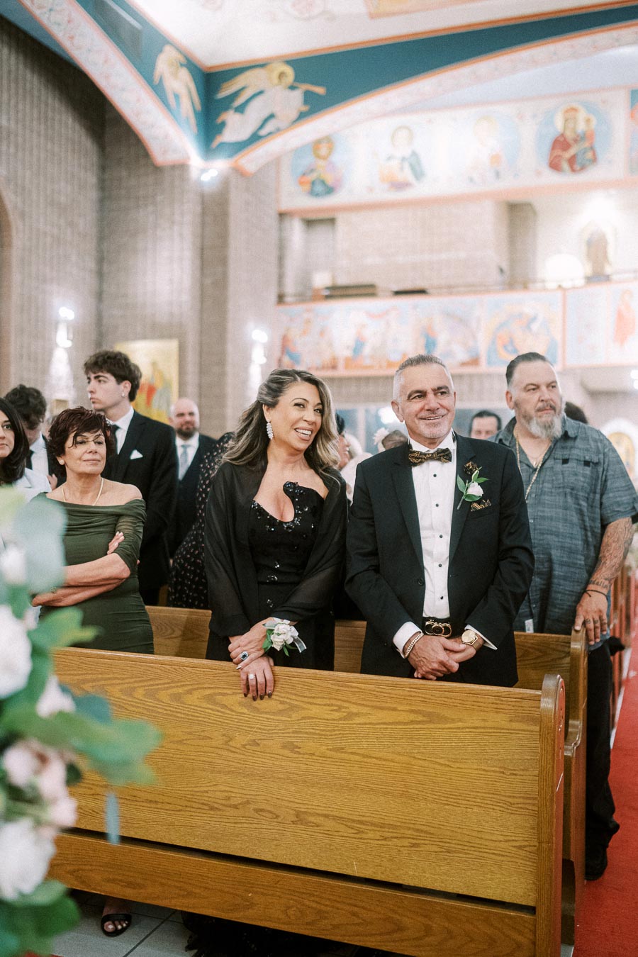 A joyful couple dressed in formal attire stands in a beautifully decorated church, surrounded by family and friends.