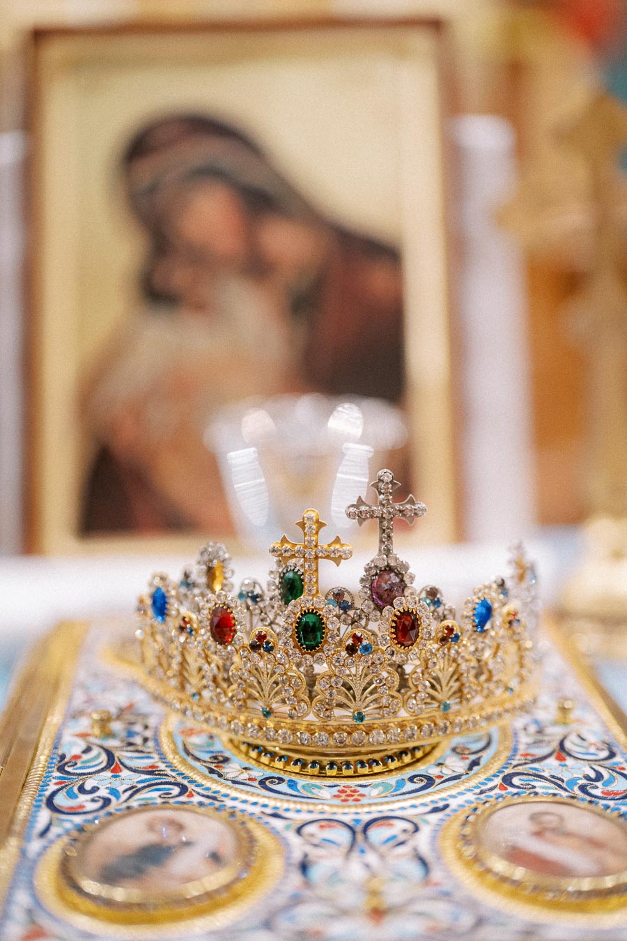 Ornate golden crown adorned with colorful gemstones and crosses, placed on an intricately designed book, with a