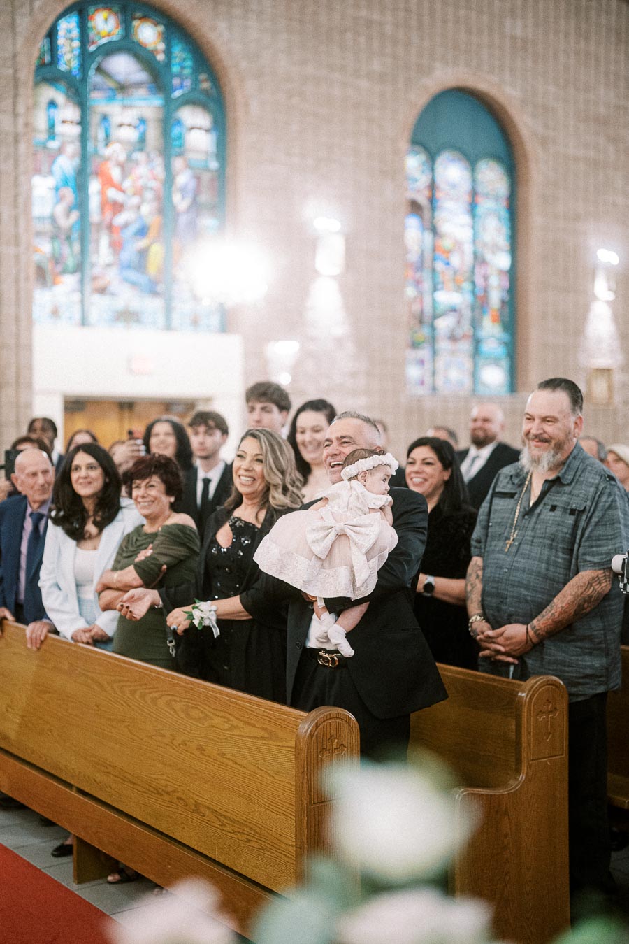 A joyful gathering of family and friends celebrating a christening in a beautifully decorated church with stained glass