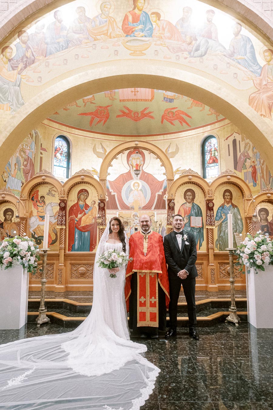 Wedding ceremony in an ornate church with a bride in a long white gown and a groom in a black suit standing beside a priest